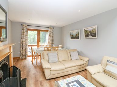 A living room with beige sofas a dining table with chairs and glass doors with curtains at 14 Sneem Leisure Village in Sneem County Kerry