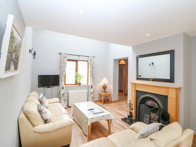 A living room with two beige sofas a coffee table a flat screen TV and a fireplace at 14 Sneem Leisure Village in Sneem County Kerry