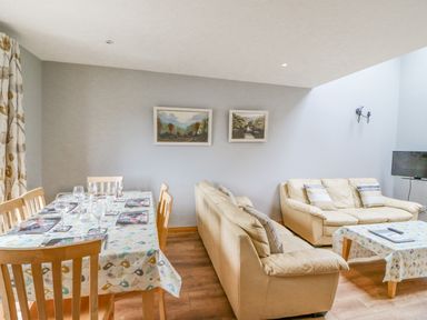 A dining area with a table set with wine glasses and a living room with two beige sofas and a wall-mounted television at 14 Sneem Leisure Village in Sneem County Kerry
