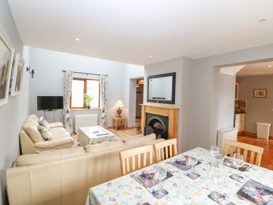 A living room with beige sofas a wooden dining table set with glassware and a fireplace at 14 Sneem Leisure Village in Sneem County Kerry