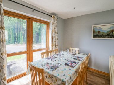 A dining room with a table set for six near wooden framed glass doors and curtains at 14 Sneem Leisure Village in Sneem County Kerry