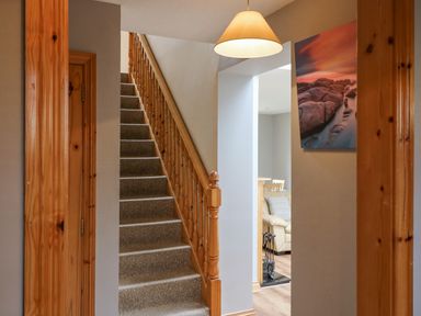A carpeted staircase with wooden handrail and beige walls with a view into a living room at 14 Sneem Leisure Village in Sneem County Kerry
