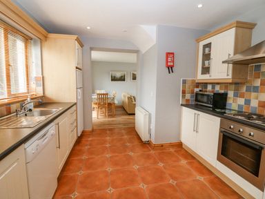 A kitchen with white cabinets tiled backsplash microwave oven dishwasher and a sink next to a window opening to a dining area at 14 Sneem Leisure Village in Sneem County Kerry