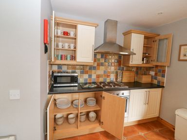 A kitchen with open cabinets showing cups plates and bowls a microwave and a stove with a tiled backsplash at 14 Sneem Leisure Village in Sneem County Kerry