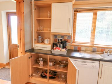 A kitchen with open cabinets showing pots pans and glassware beside a window and dishwasher at 14 Sneem Leisure Village in Sneem County Kerry