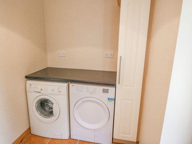 A laundry room with a washing machine and dryer under a countertop next to a tall cabinet at 14 Sneem Leisure Village in Sneem County Kerry