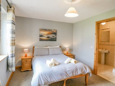 A bedroom with a bed pillows and rolled towels two bedside tables with lamps and a bathroom visible through an open door at 14 Sneem Leisure Village in Sneem County Kerry