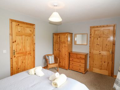 A bedroom with two wooden doors a wooden wardrobe a wooden dresser a wicker chair and a bed with folded white towels at 14 Sneem Leisure Village in Sneem County Kerry