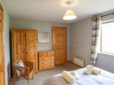 A bedroom with wooden wardrobe dresser and chair next to a bed with folded towels at 14 Sneem Leisure Village in Sneem County Kerry