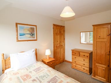 A bedroom with a single bed bedside table lamp wooden chest of drawers wardrobe and a framed painting at 14 Sneem Leisure Village in Sneem County Kerry