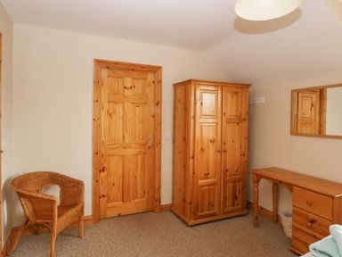 A room with a wooden door a wicker chair a wooden wardrobe a wooden desk with drawers and a mirror on the wall at 14 Sneem Leisure Village in Sneem County Kerry