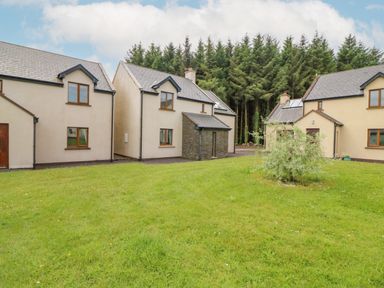 A group of cream houses with slate roofs around a green lawn and trees in the background at 14 Sneem Leisure Village in Sneem County Kerry