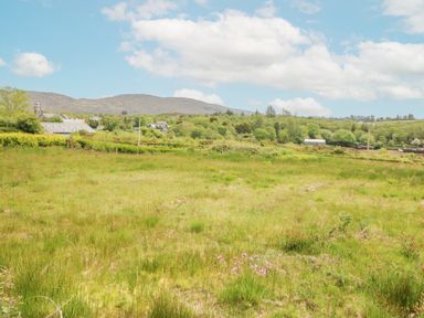 A grassy field with wildflowers and bushes with houses and hills in the background at 14 Sneem Leisure Village in Sneem County Kerry