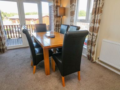 A dining area with a wooden table and six black chairs near windows and a balcony door at Gressingham 22 in South Lakeland Leisure Village