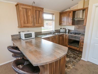 A kitchen with wooden cabinets a countertop with two bar stools a microwave toaster kettle gas stove and oven at Gressingham 22 South Lakeland Leisure Village
