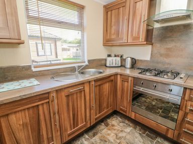A kitchen with wooden cabinets a sink a gas stove a toaster and a kettle at Gressingham 22 South Lakeland Leisure Village