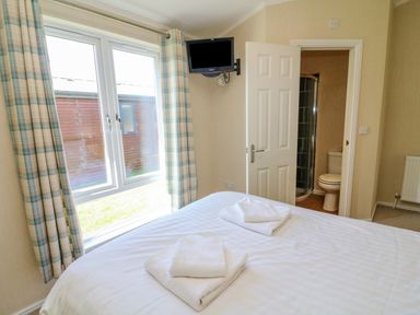 A bedroom with a bed and folded towels near a window and a door leading to a bathroom at Gressingham 22 in South Lakeland Leisure Village