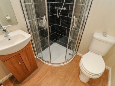A bathroom with a corner shower, a white toilet, and a sink with a wooden cabinet at Gressingham 22 South Lakeland Leisure Village