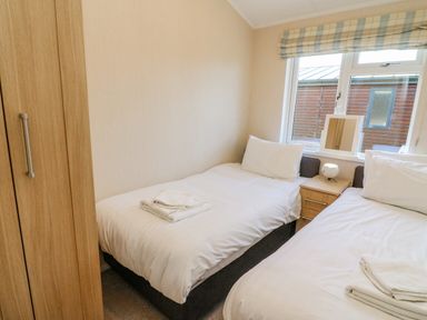 A bedroom with two single beds a wooden wardrobe and a window at Gressingham 22 in South Lakeland Leisure Village