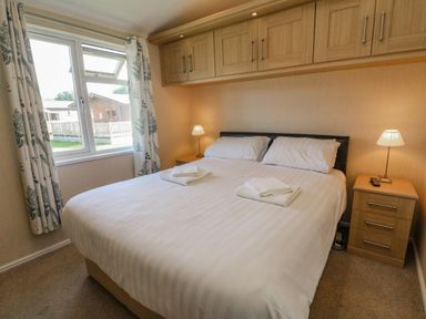 A bedroom with a double bed bedside tables lamps and overhead cabinets at Gressingham 22 in South Lakeland Leisure Village