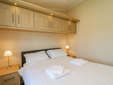 A bedroom with a double bed white linens two bedside tables with lamps and overhead cabinets at Gressingham 22 South Lakeland Leisure Village