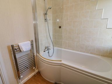 A bathroom with a bathtub and showerhead next to a towel rack with a white towel at Gressingham 22 in South Lakeland Leisure Village