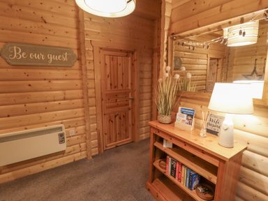A hallway with wooden walls and door a wooden shelf with books a lamp and a mirror above at Leafy Hollow Lodge in Louth