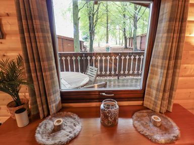 A wooden table with plaid curtains on either side and a window view of a wooden balcony and trees at Leafy Hollow Lodge in Louth