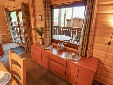 A wooden dining chair next to a sideboard with decorative items and a window with curtains showing an outdoor table at Leafy Hollow Lodge in Louth