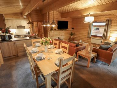 A dining table set with dishes and glasses in an open plan kitchen and living area with sofas and a wall mounted TV at Leafy Hollow Lodge in Louth