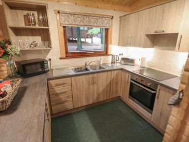 A kitchen with wooden cabinets a microwave a double sink an oven a toaster and a window at Leafy Hollow Lodge in Louth