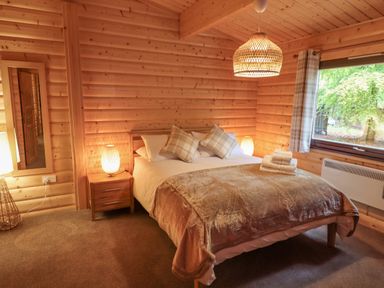 A bedroom with a double bed bedside tables lamps a window and wooden walls at Leafy Hollow Lodge in Louth