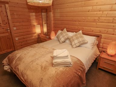 A bedroom with a double bed two plaid pillows bedside lamps folded towels on bed wooden wall panels at Leafy Hollow Lodge in Louth