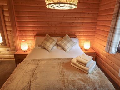 A bedroom with a bed with pillows and folded towels on a blanket at Leafy Hollow Lodge in Louth