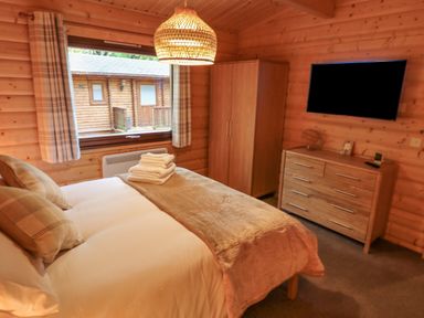 A bedroom with a double bed pillows folded towels window wardrobe chest of drawers and wall mounted tv at Leafy Hollow Lodge in Louth