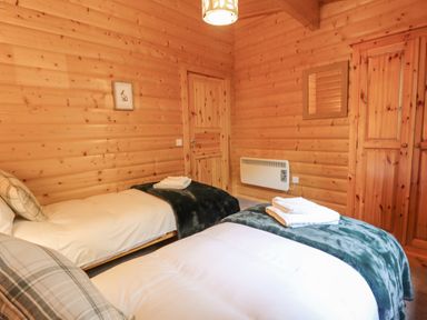 A bedroom with two single beds wooden walls a door a wardrobe and a wall mirror at Leafy Hollow Lodge in Louth