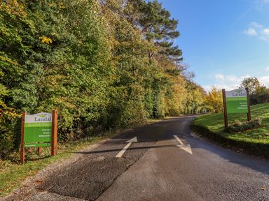 A road with directional arrows and green signs reading Landal Kenwick Woods surrounded by trees at Leafy Hollow Lodge in Louth
