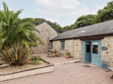 An outdoor patio area with stone buildings blue doors picnic table and plants at Pendeen in Mawnan Smith Near Falmouth