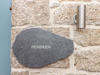 A stone wall with a black stone plaque reading Pendeen and a metal light fixture at Pendeen in Mawnan Smith Near Falmouth