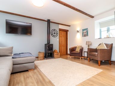 A living room with a gray sofa a wood burning stove and two brown armchairs at Pendeen in Mawnan Smith Near Falmouth