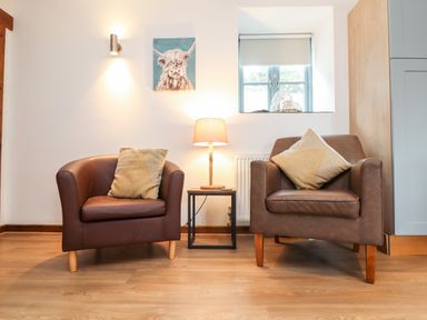A seating area with two brown leather chairs a small table with a lamp a painting on the wall and a window at Pendeen in Mawnan Smith Near Falmouth