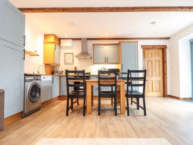 A kitchen with wooden flooring a dining table with four black chairs and light blue cabinets at Pendeen in Mawnan Smith Near Falmouth