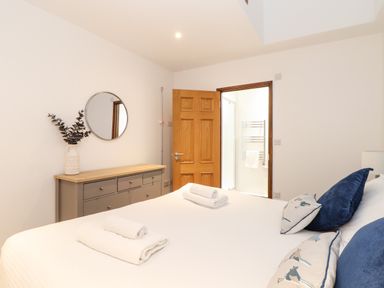 A bedroom with a bed and pillows and a dresser with a mirror and vase at Pendeen in Mawnan Smith Near Falmouth
