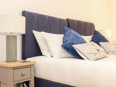 A bedroom with a bed with blue headboard and pillows and bedside tables with lamps at Pendeen in Mawnan Smith Near Falmouth