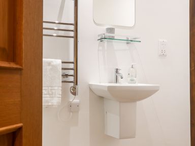 A bathroom with a white sink and faucet a glass shelf with a container a chrome towel rack with a white towel and a wooden door at Pendeen in Mawnan Smith Near Falmouth