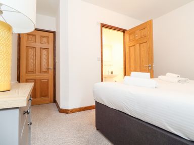 A bedroom with a bed with towels a wooden door open to a bathroom and a chest of drawers with a lamp at Pendeen in Mawnan Smith Near Falmouth