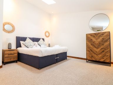 A bedroom with a large bed bedside tables lamps wooden dresser and round mirrors at Pendeen in Mawnan Smith Near Falmouth