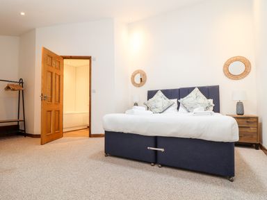 A bedroom with a double bed two side tables lamps and an open door showing a bathroom at Pendeen in Mawnan Smith Near Falmouth