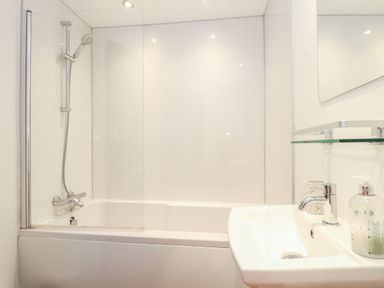 A bathroom with a bathtub shower combination and a sink with soap dispenser at Pendeen in Mawnan Smith Near Falmouth