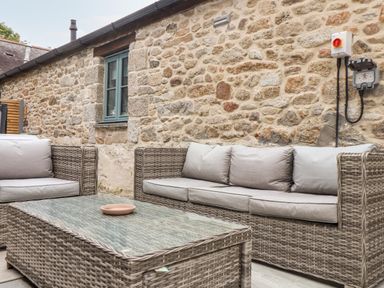 An outdoor seating area with wicker sofas and a glass coffee table against a stone wall at Pendeen in Mawnan Smith Near Falmouth